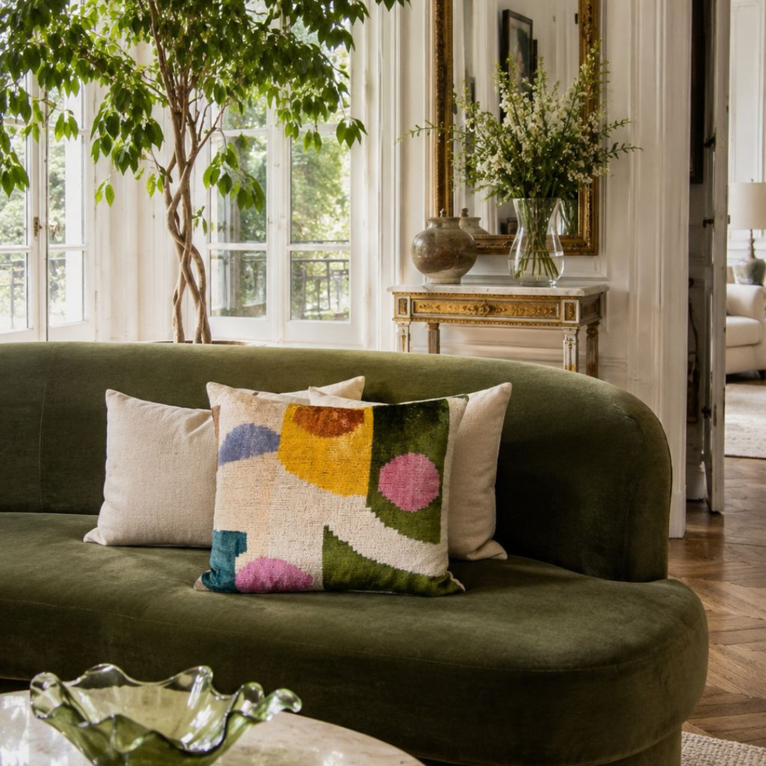 Handmade Carnival silk velvet ikat pillow cover featuring pink, green, yellow and blue abstract design styled on a green velvet sofa in an elegant living room.