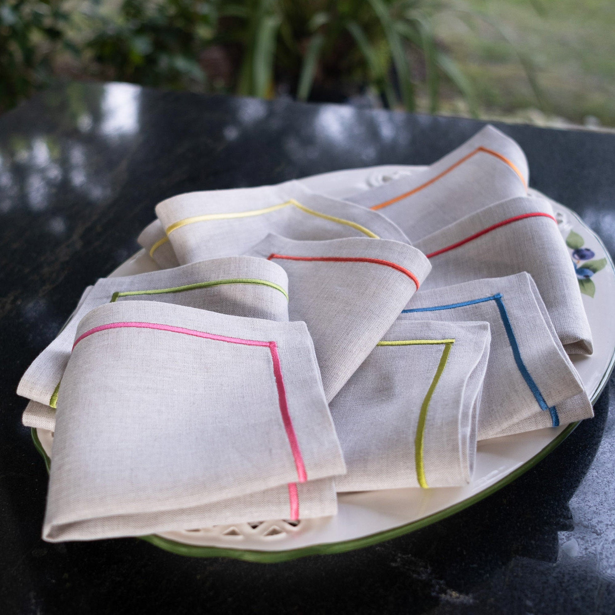 Elegant linen cocktail napkins with colorful embroidered borders styled on a dessert table in the garden