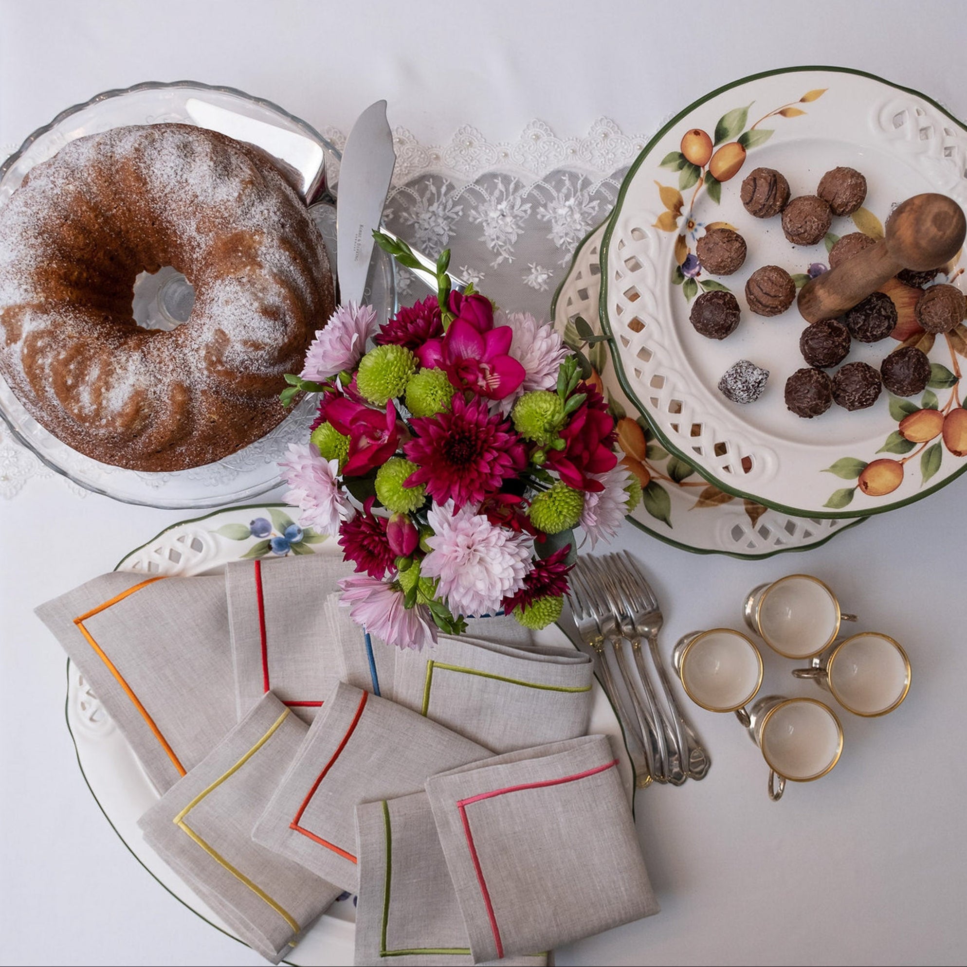Elegant linen cocktail napkins with colorful embroidered borders styled on a spring table setting with flowers, desserts, and vintage plates