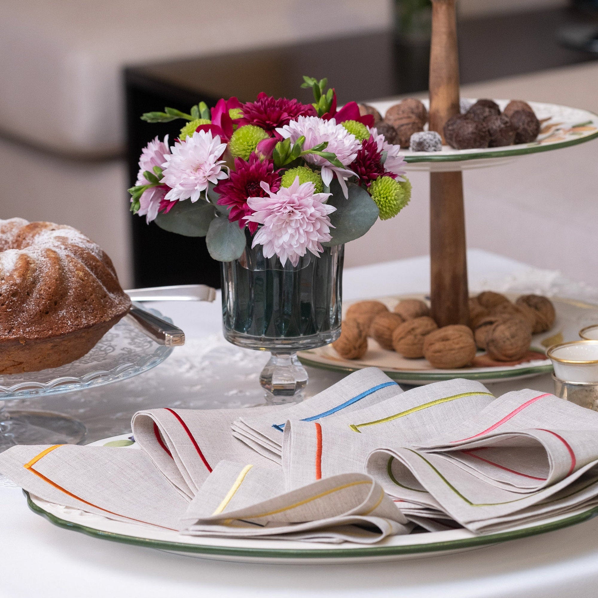 Elegant linen cocktail napkins with colorful embroidered borders styled on a dessert table with flowers and pastries