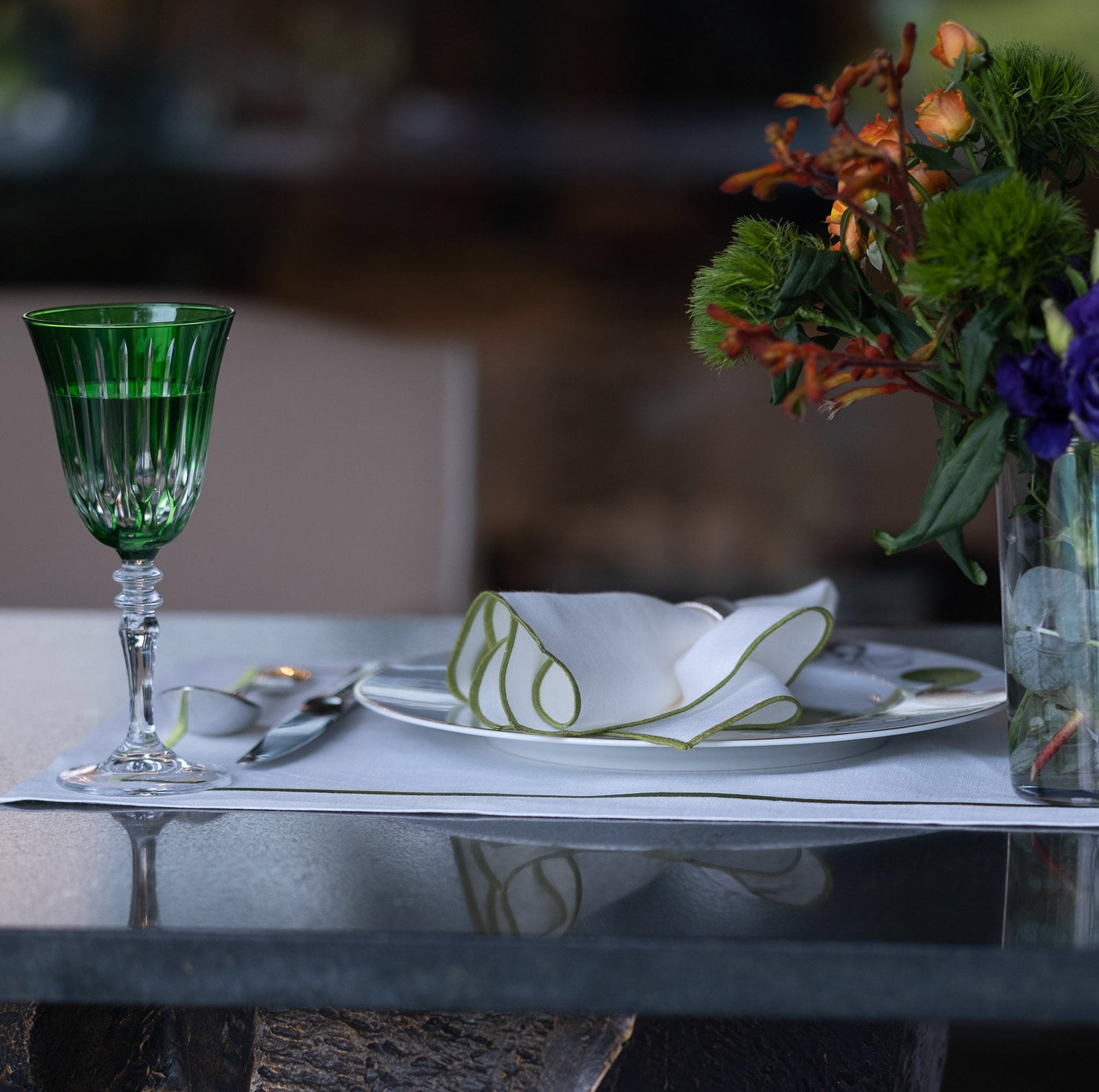 Elegant white linen napkin with green stitched edges styled on a refined table setting with vibrant floral arrangements, crystal glassware, and timeless entertaining details.