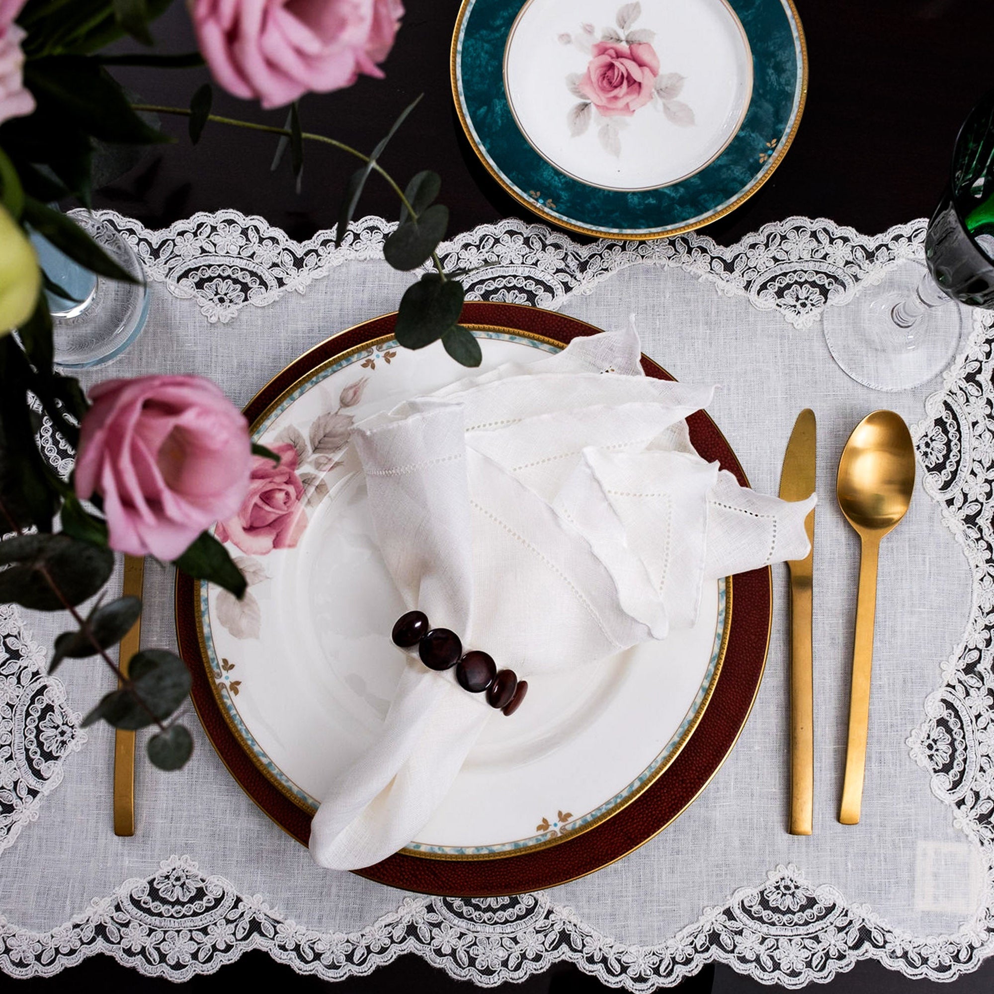 Elegant white linen napkin with ruffle hemstitched edges, styled on a blue patterned dinner plate with matching blue bordered placemat.
