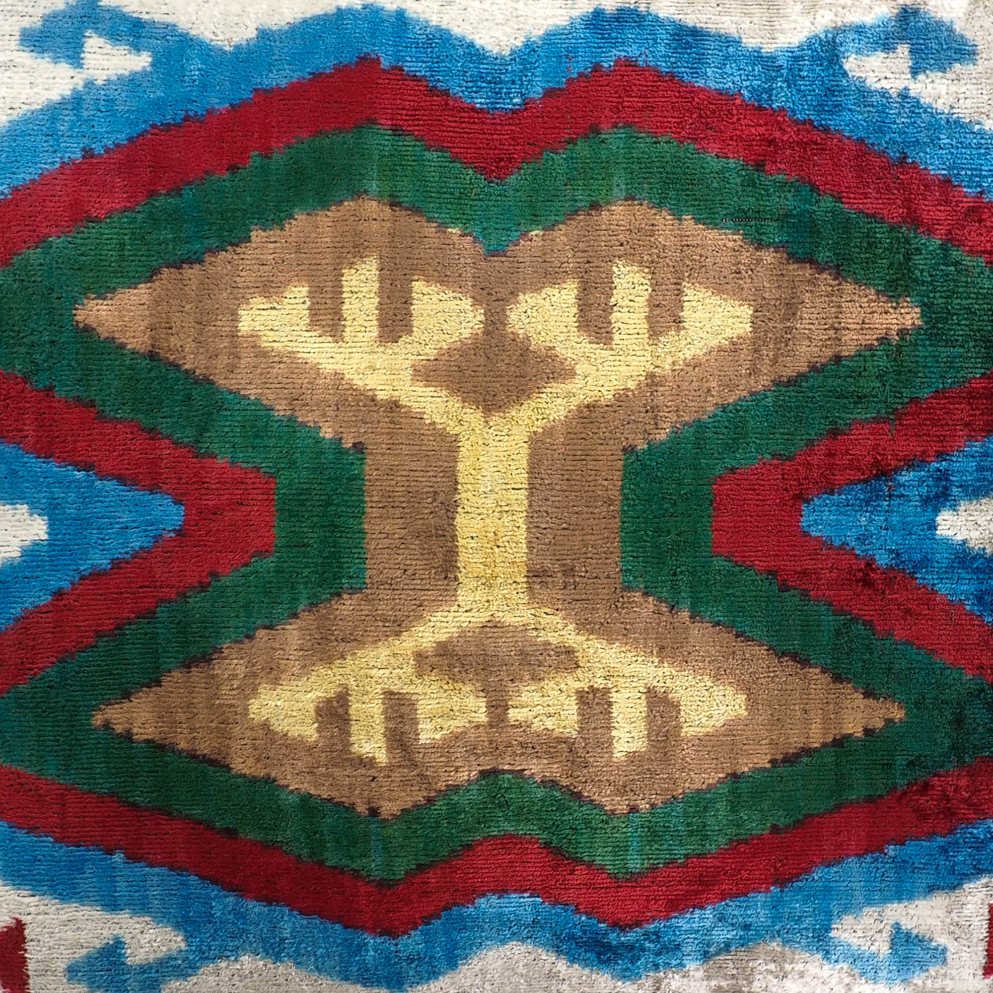 Artisanal silk velvet cushion in multicolor zigzag design with bold central tribal symbol.