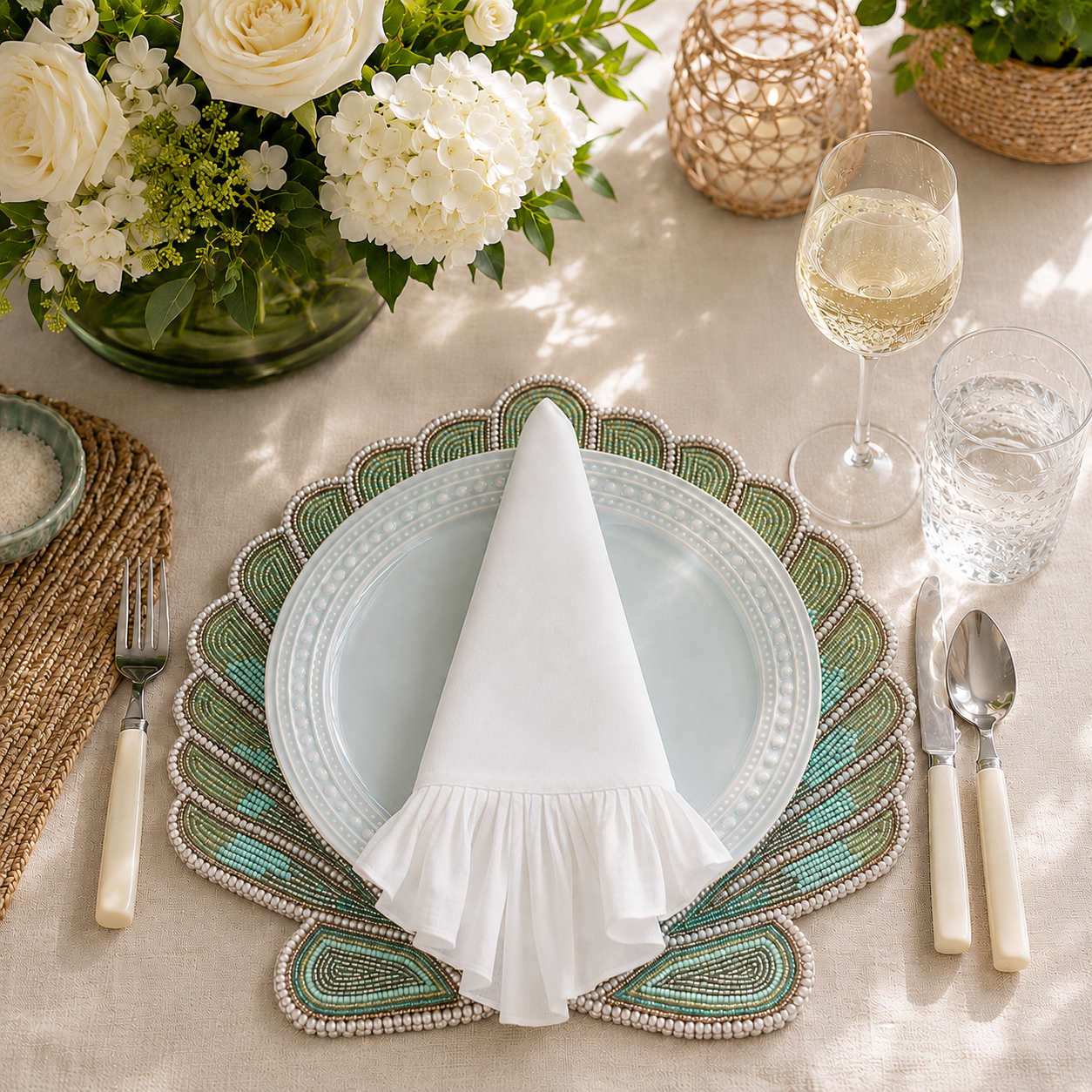 ChouChou Touch white pleated-edge linen napkin styled on a pale blue plate with a green and turquoise beaded placemat and elegant floral table setting.