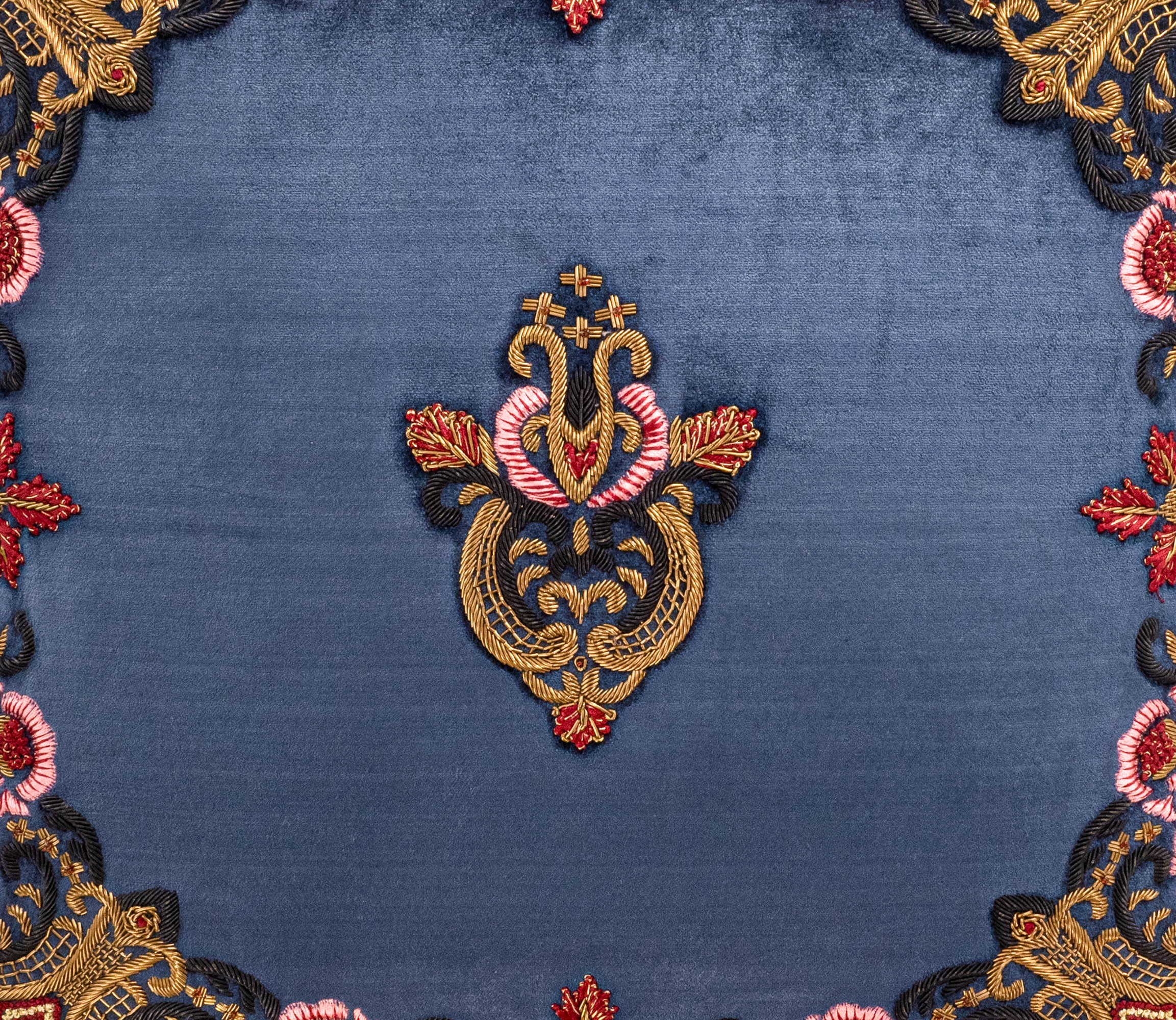 Close-up of ChouChou Touch's Regina Collection blue silk velvet pillow featuring detailed red, pink and gold baroque embroidery with regal crest and decorative tassel.