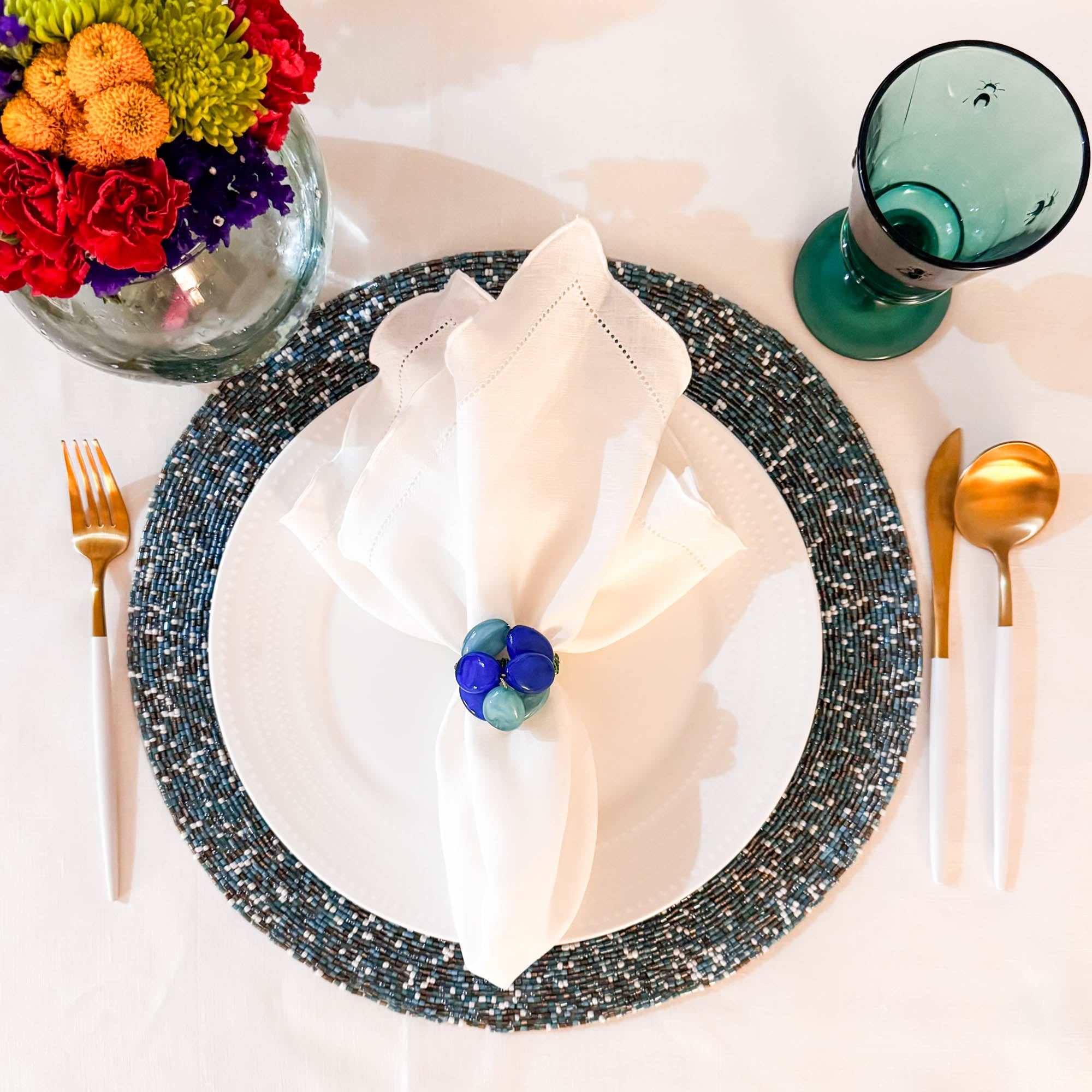 Elegant table setting featuring seaside glass beaded placemat with white linen napkin and gold cutlery by ChouChou Touch