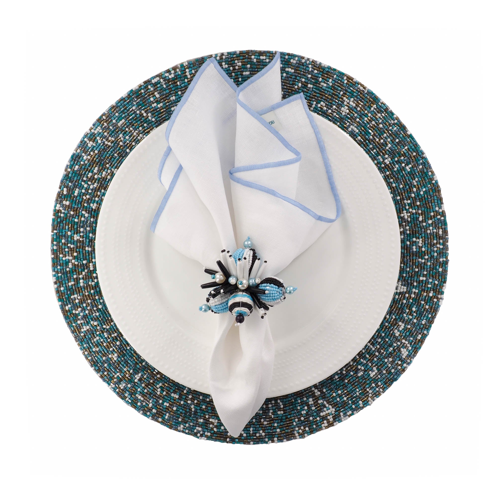 Coastal- inspired dining table with ChouChou Touch seaside beaded placemats, white napkin with blue stitched edges, and elegant white, black and blue napkin ring