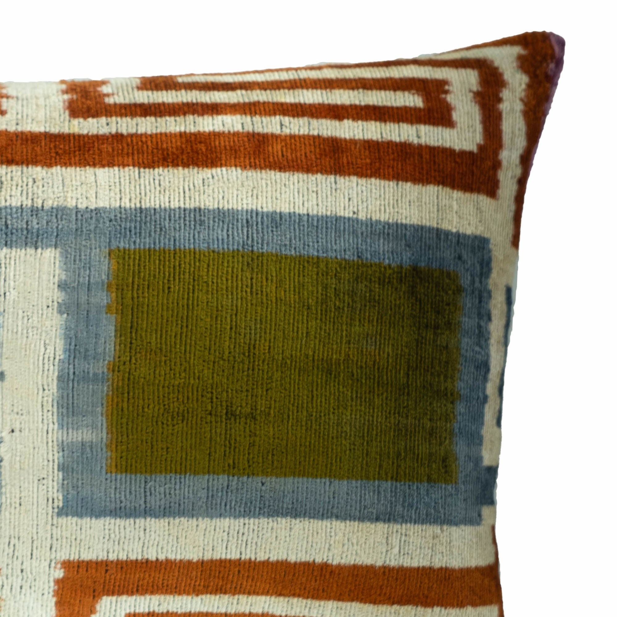 Close-up of handmade silk velvet ikat fabric featuring intricate geometric motifs in olive green, blue, and rust tones with luxurious velvet texture.