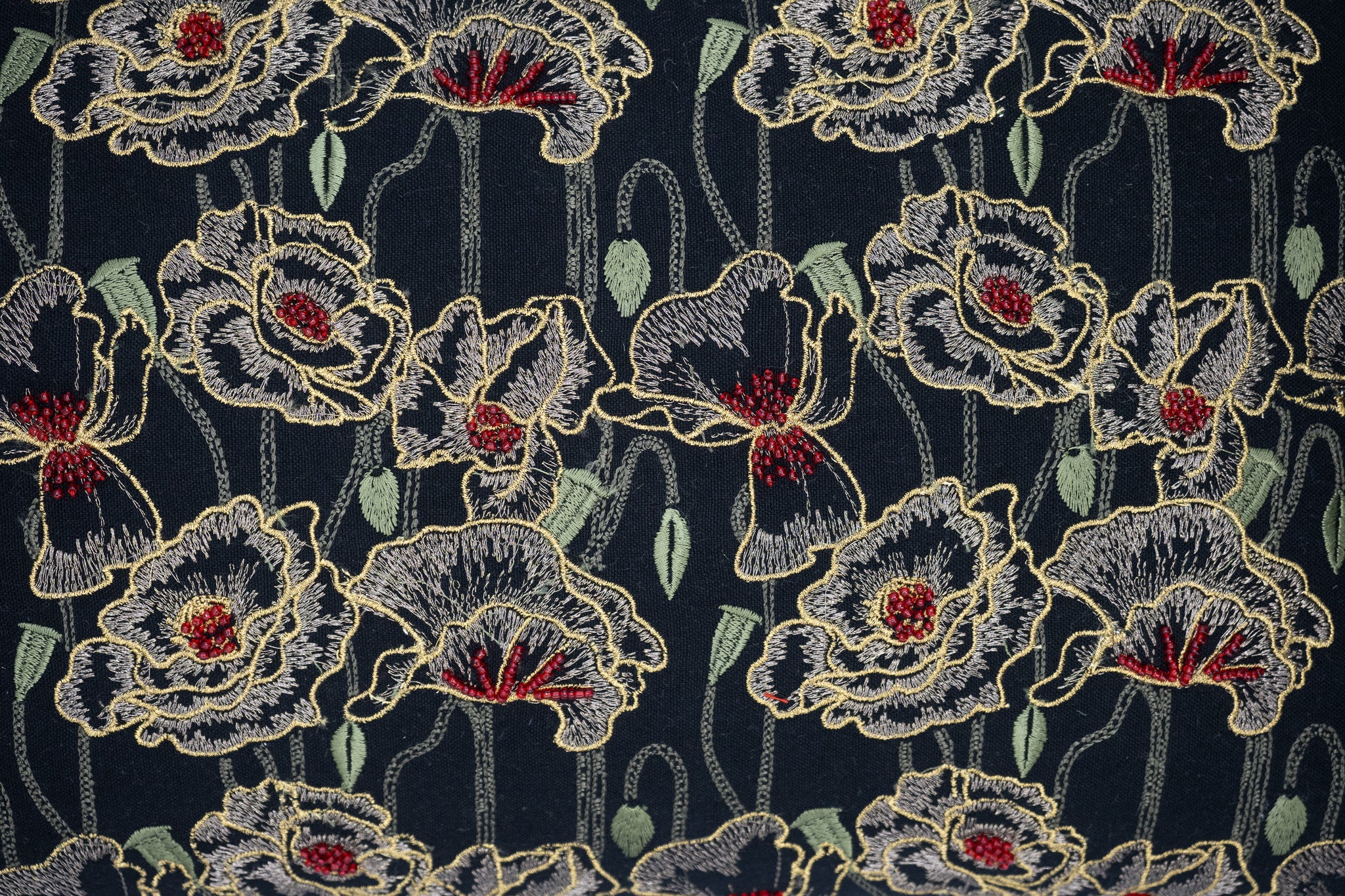Luxury embroidered sofa pillow with golden orchids and sage vines on black fabric.