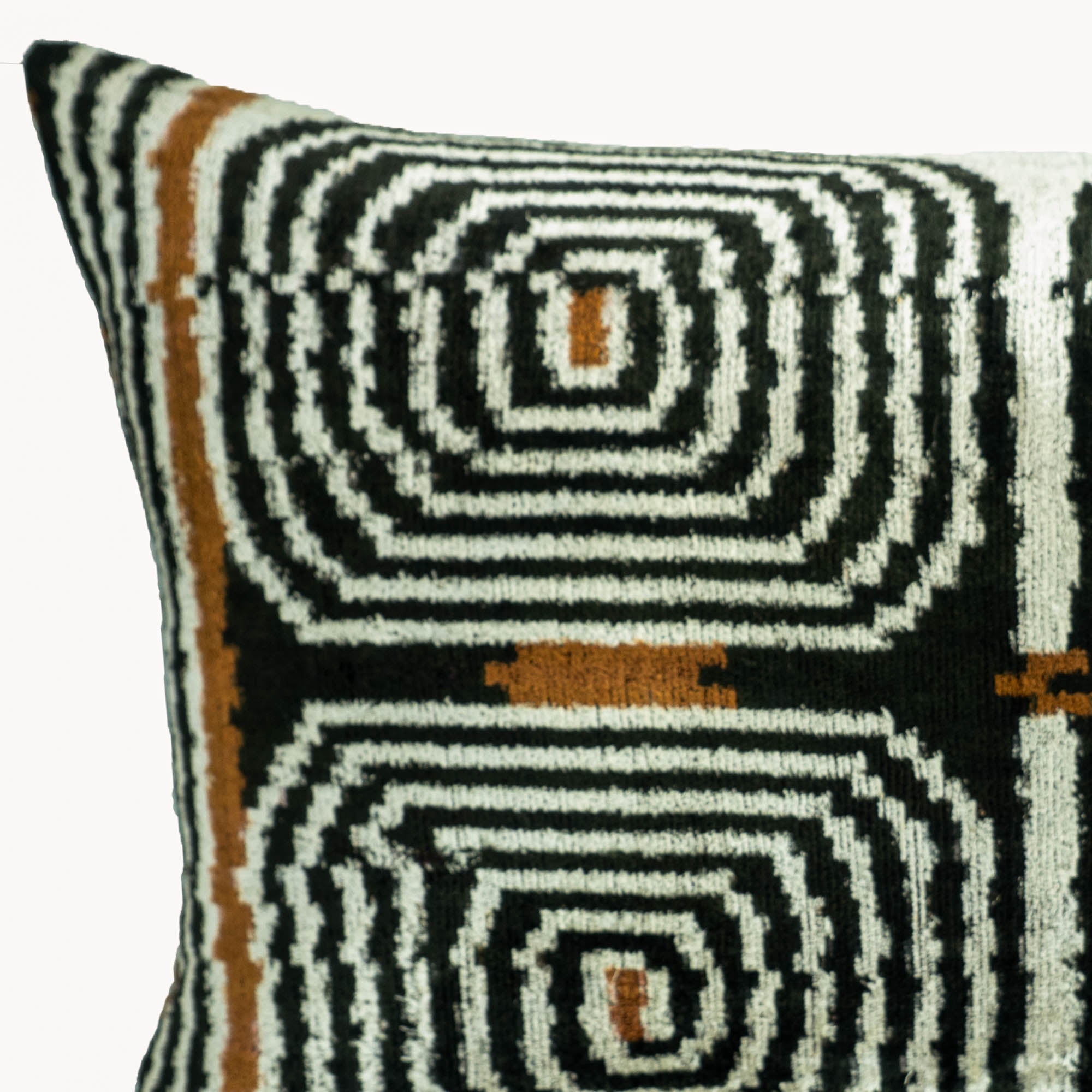 Close-up of a handwoven silk velvet ikat pillow cover featuring a black, ivory and bronze geometric labyrinth pattern inspired by traditional Uzbek weaving.
