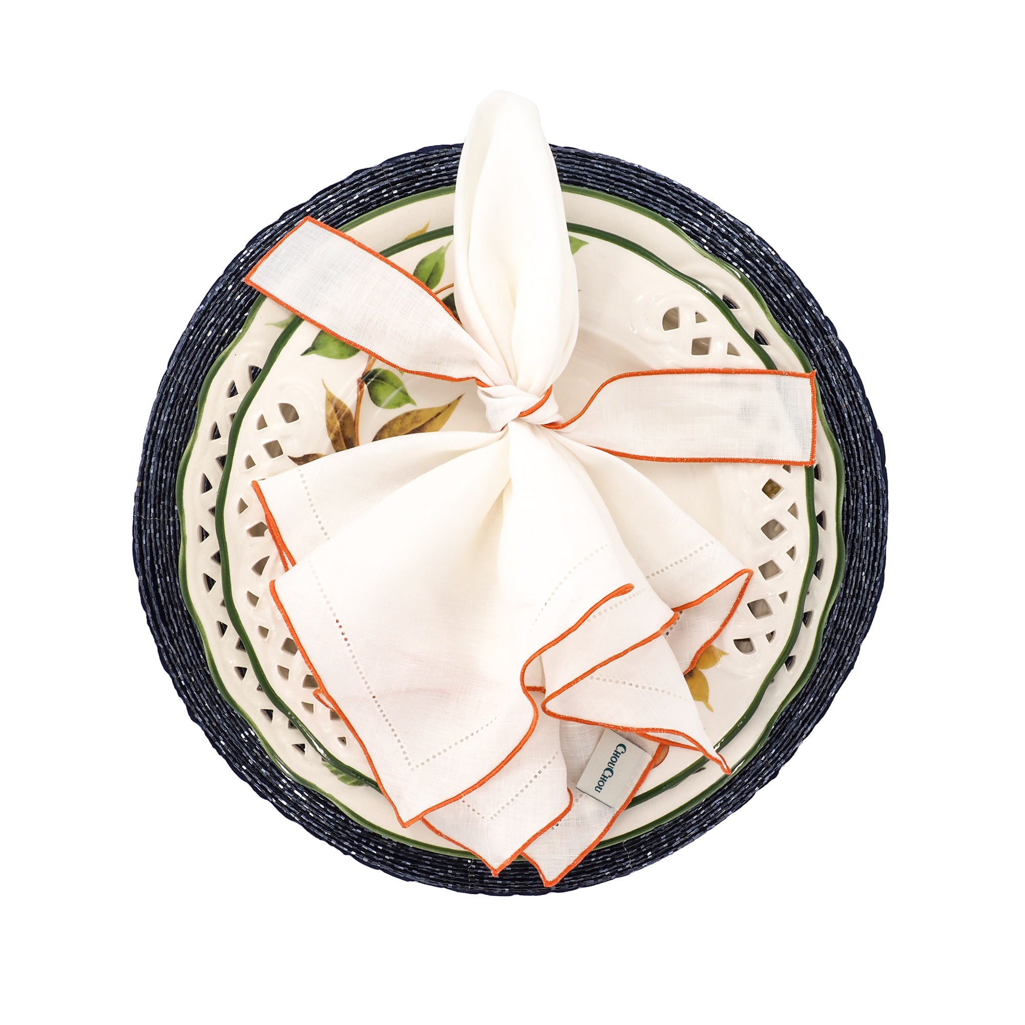 White linen napkins with orange ruffled hemstitched edge styled in a knot on a decorative plate and navy blue beaded placemat elegant table decor