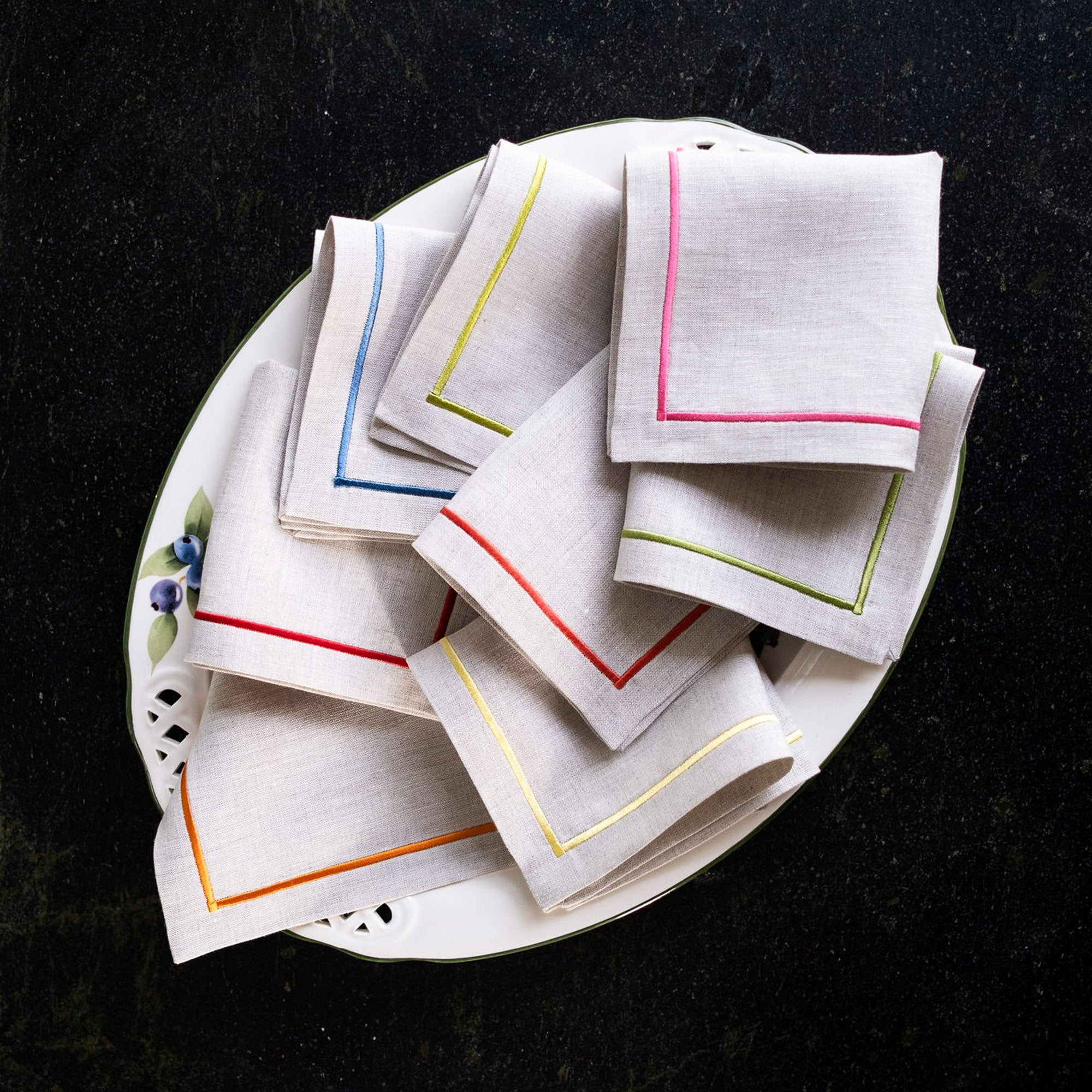 Handmade colorful linen cocktail napkins with embroidered borders styled on a white plate for elegant entertaining and table settings