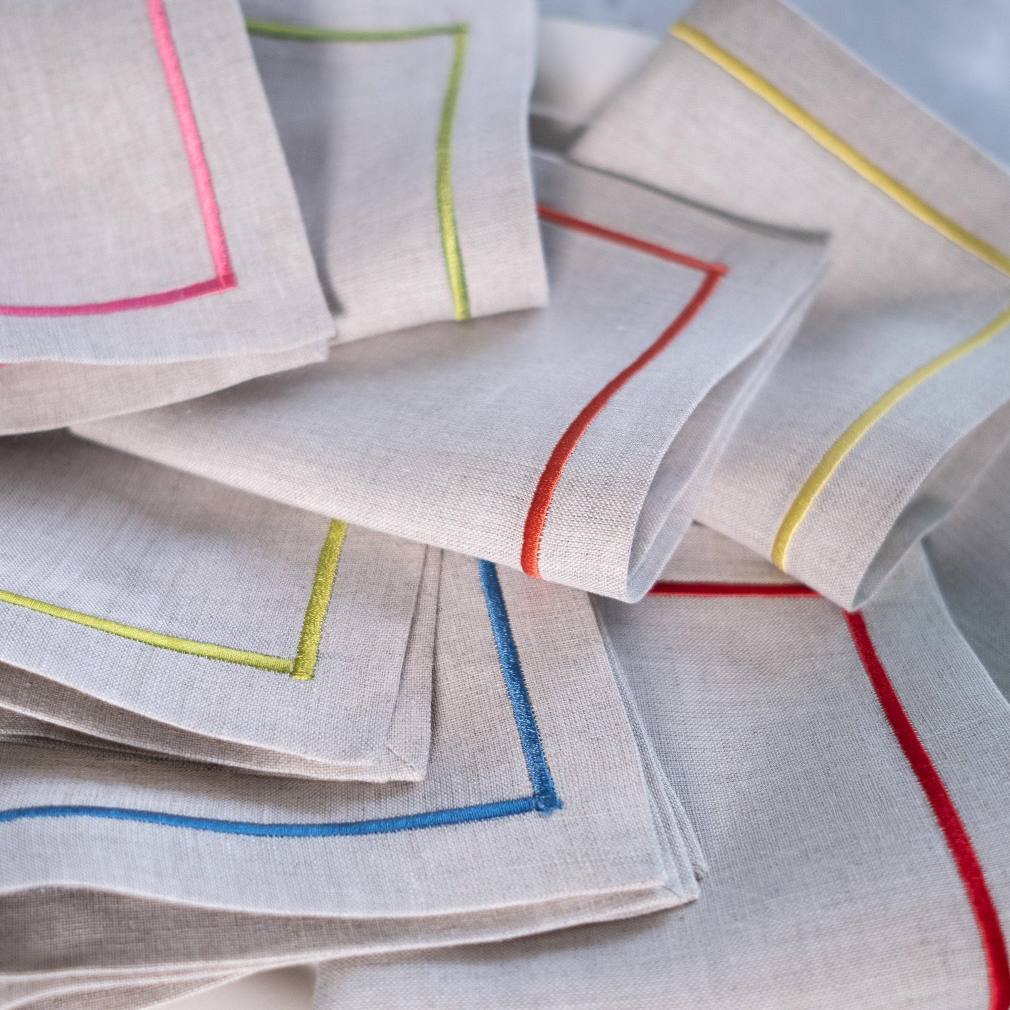 Close-up of linen cocktail napkins with colorful embroidered borders in pink, blue, yellow, green, orange and red
