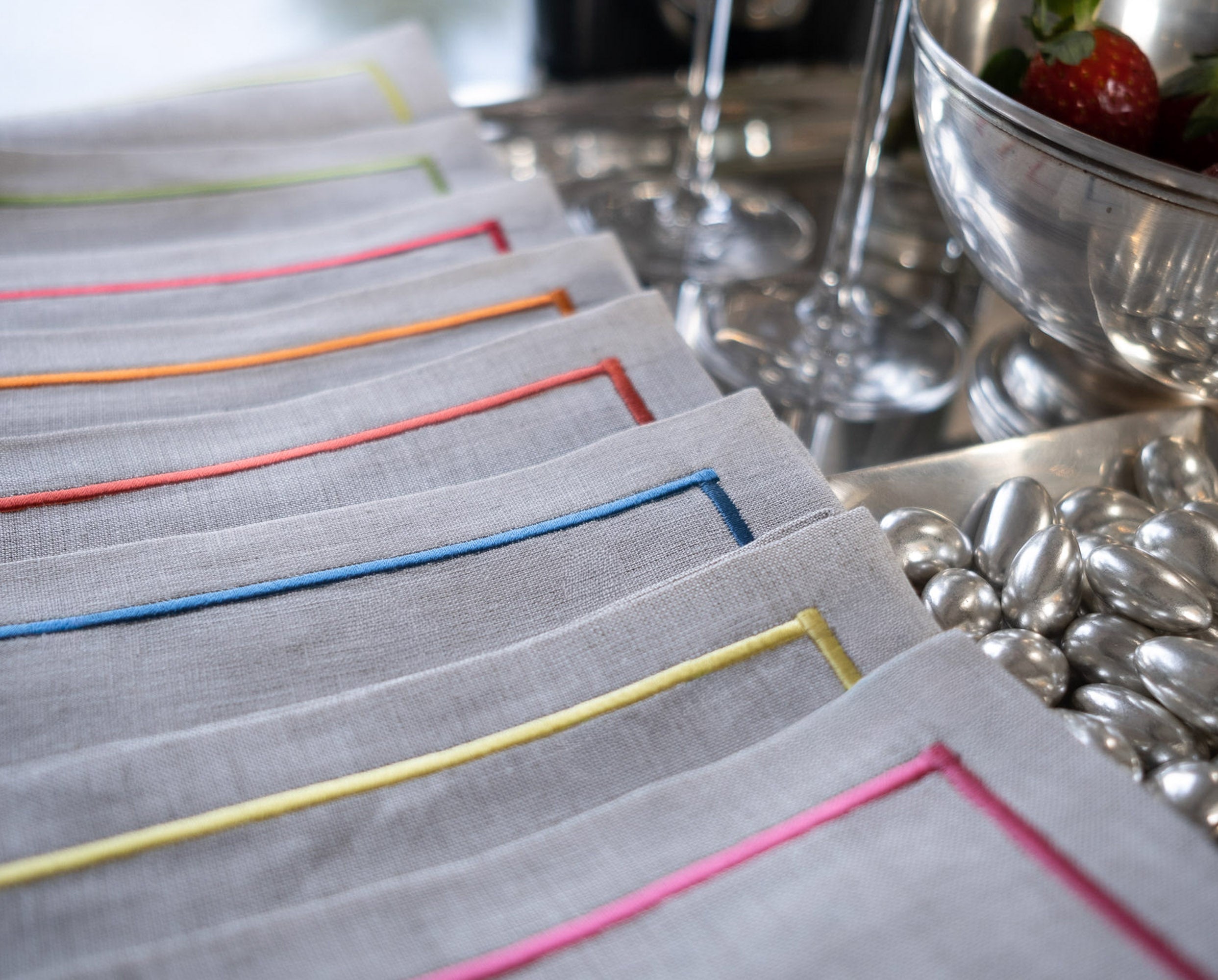 Close-up of linen cocktail napkins with colorful embroidered borders in pink, blue, orange, red, yellow, and green