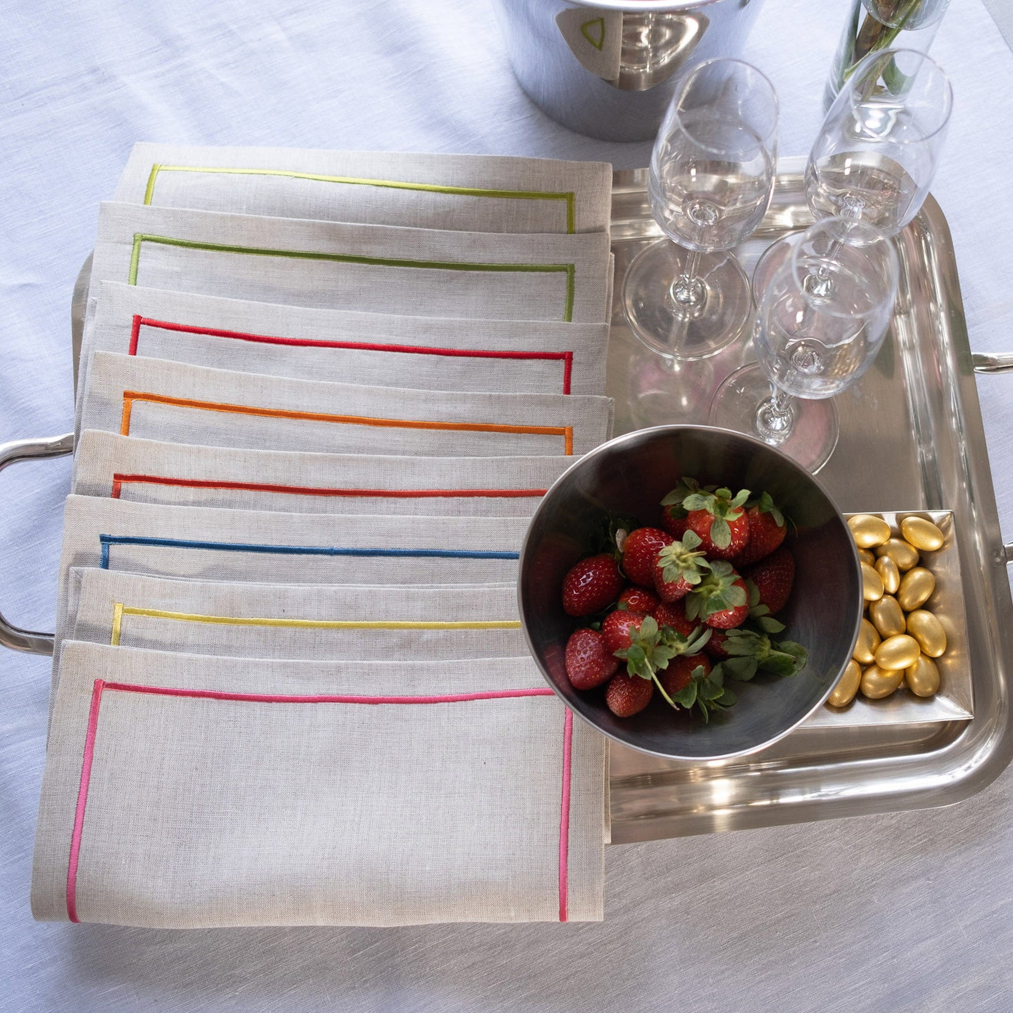 Linen cocktail napkins with colorful embroidered borders styled on a serving tray with strawberries and glassware
