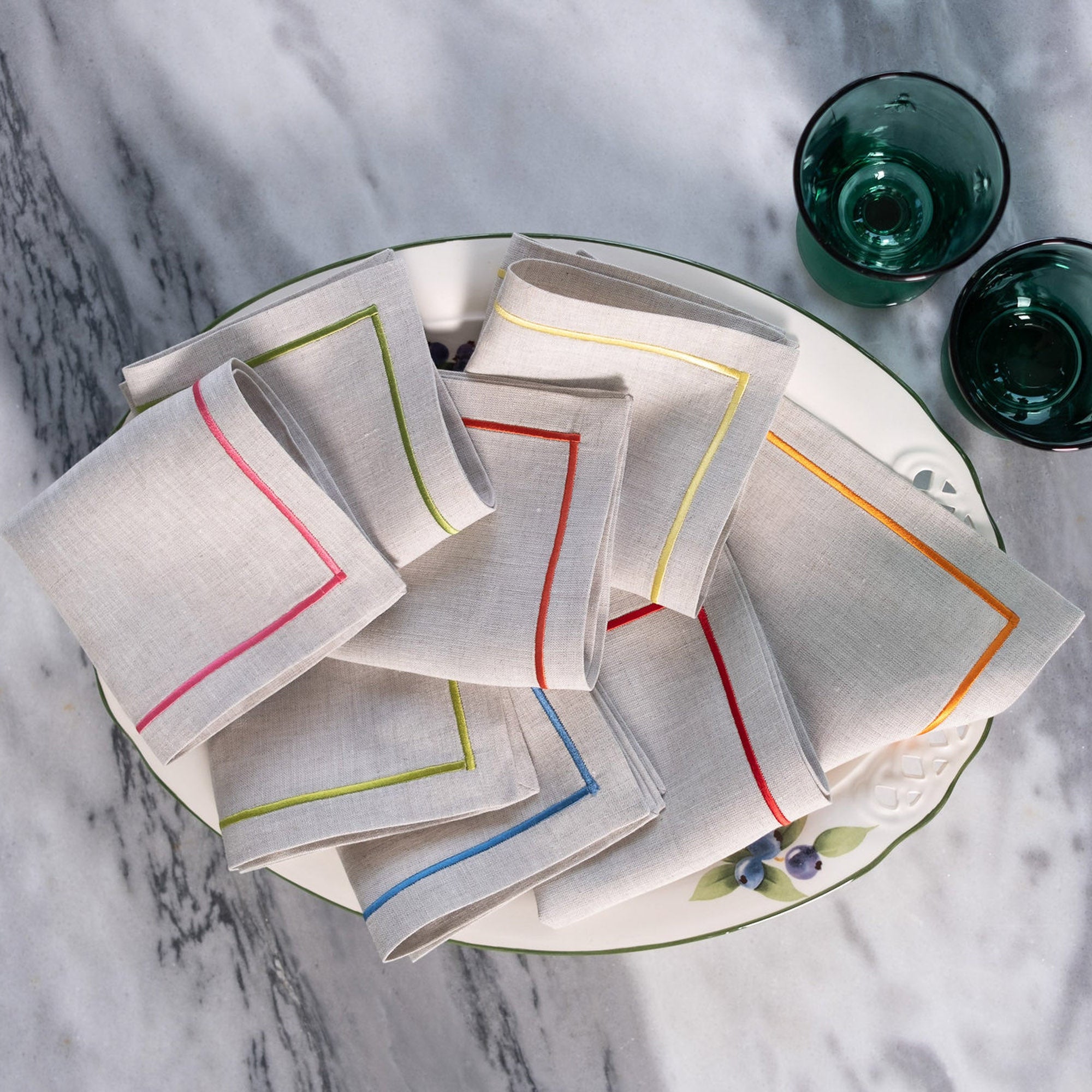 Colorful linen cocktail napkins with embroidered borders styled on a white plate for elegant entertaining and table settings