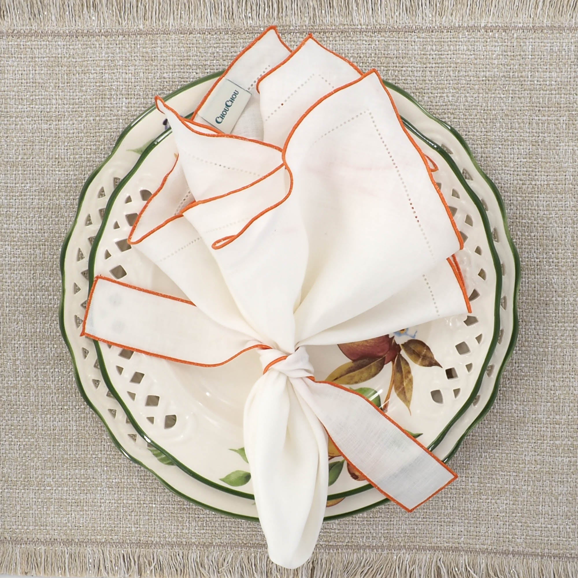 White linen napkins with orange ruffled hemstitch edges, crafted to bring a lively and sophisticated touch to your table settings.